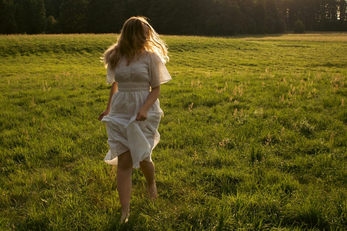 Grounding : femme marchant pieds nus dans un champ herbeux ensoleillé