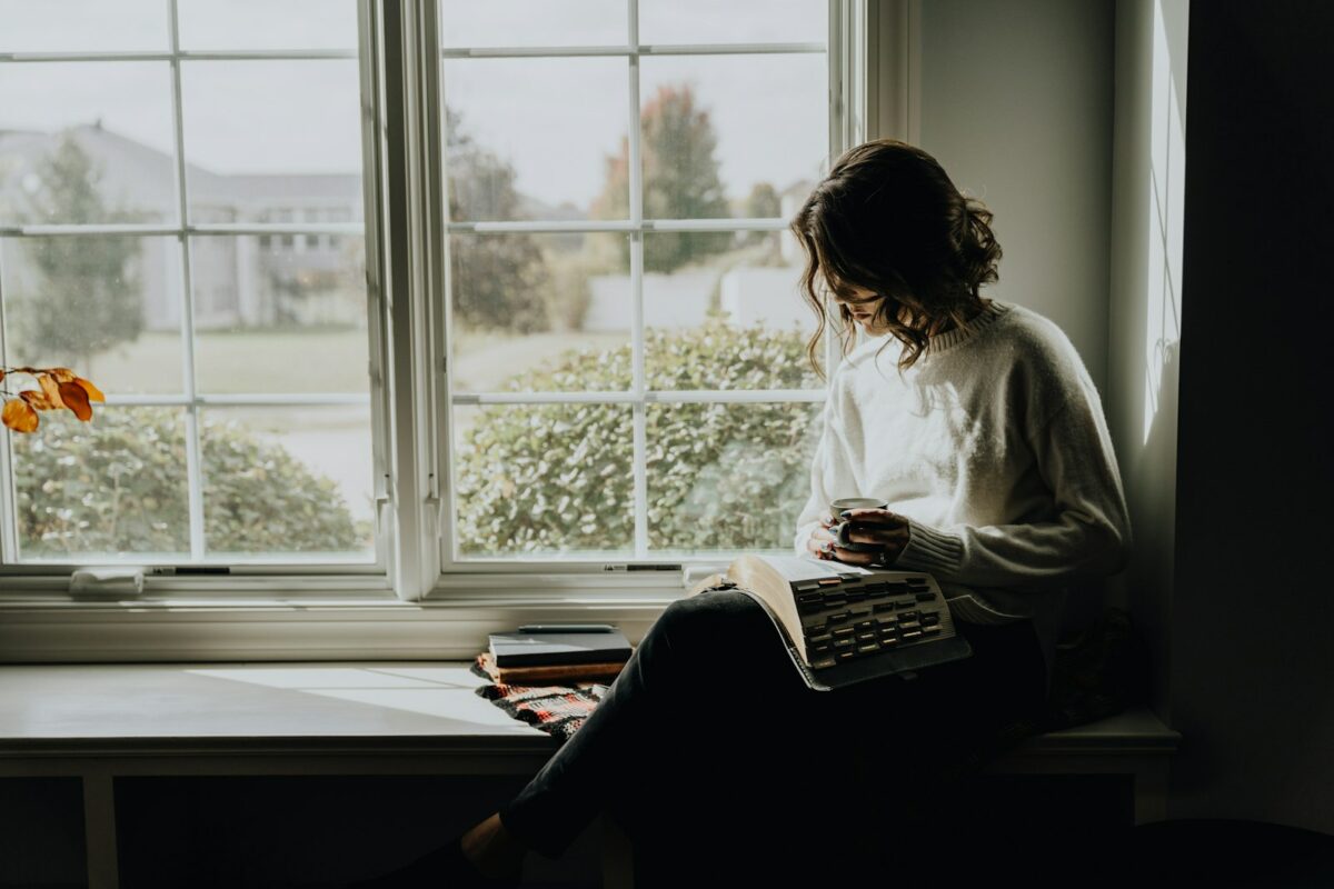 Femme en pull blanc lisant avec une tasse : la solitude choisie, un temps pour soi