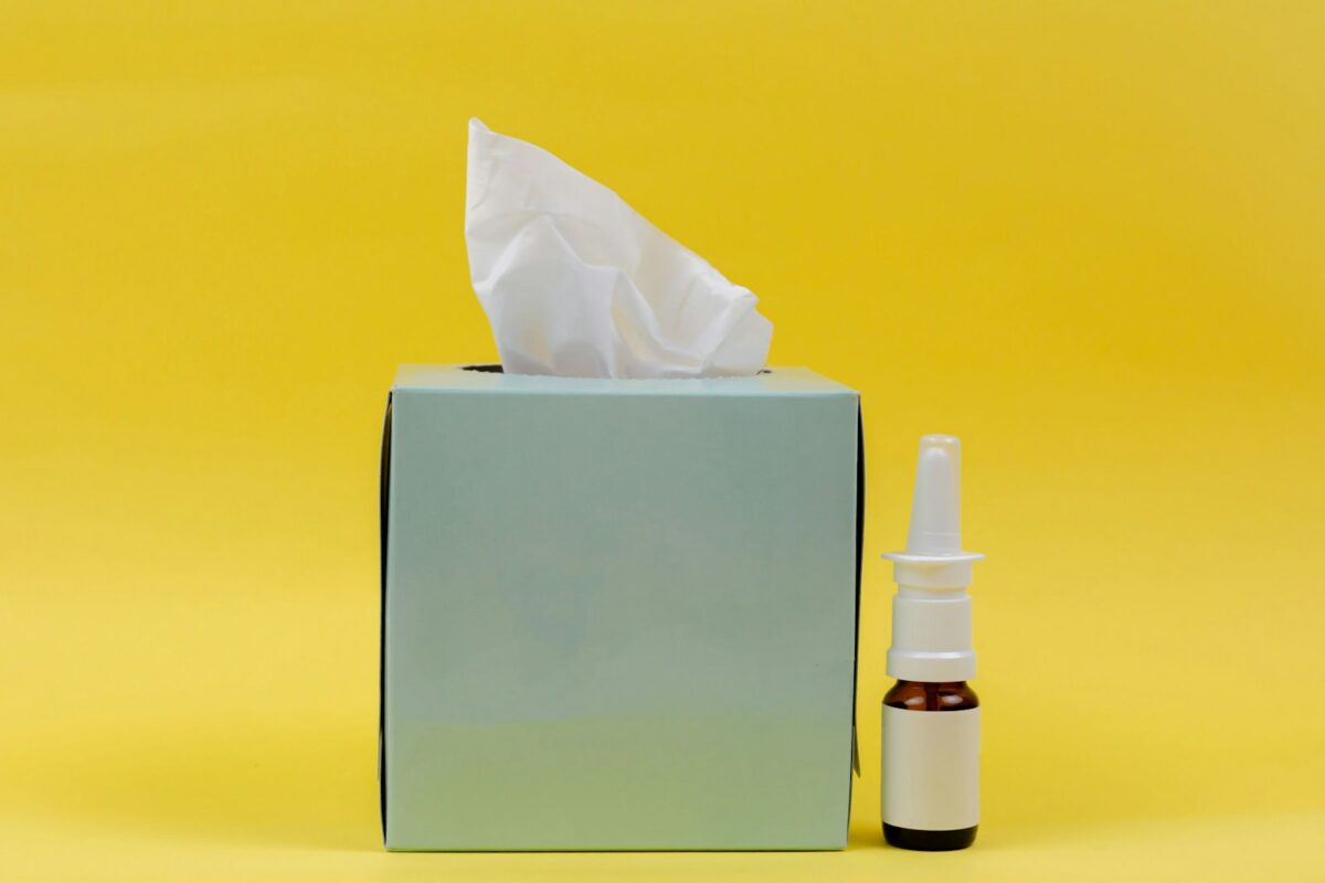 Spray nasal décongestionnant et mouchoirs en papier posés sur un fond jaune