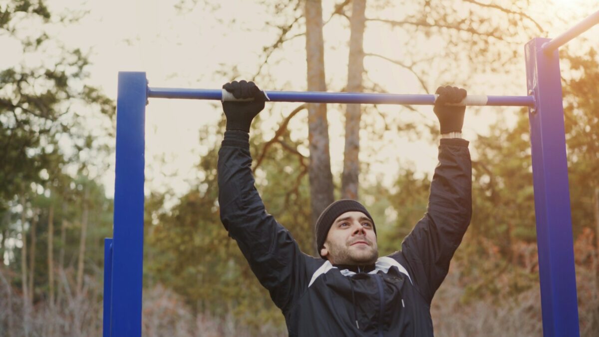 Suspension à la barre fixe : sportif accroché à une barre en extérieur